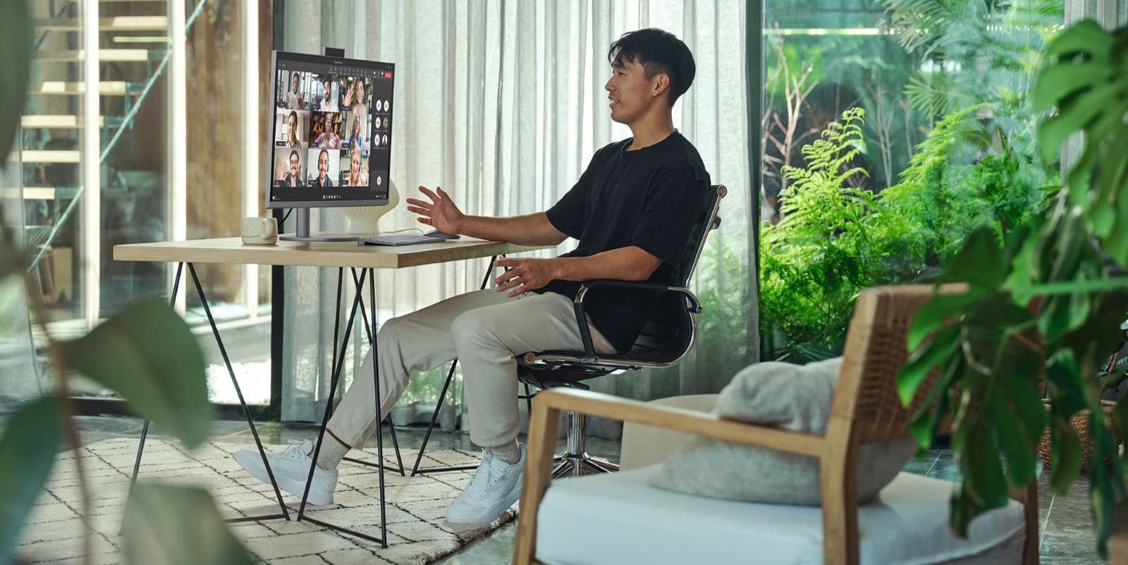 A person sitting at a desk in a bright, modern workspace having a video conference call on an HP OmniStudio X 31.5 inch All-in-One Desktop AI PC. The individual is engaging with multiple participants visible on the desktop computer